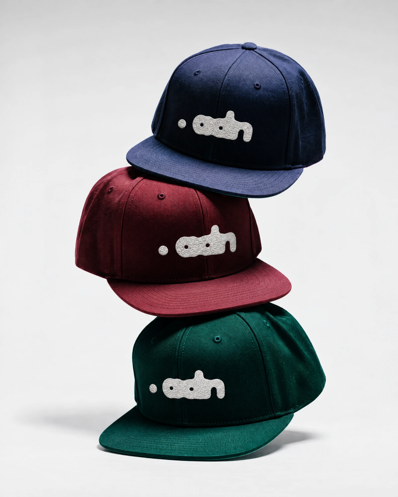 Tres gorras apiladas en azul noche, vino y pino, con el logotipo bordado en plata